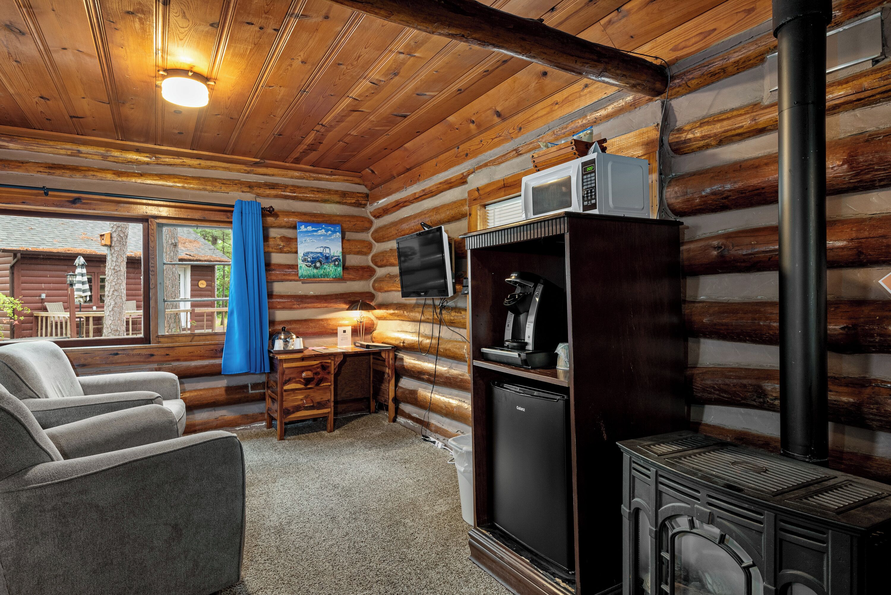 Ein Holzblockhaus-Interieur mit einer Couch, einem kleinen Tisch, einem Kühlschrank, einer Mikrowelle und einem Holzofen.