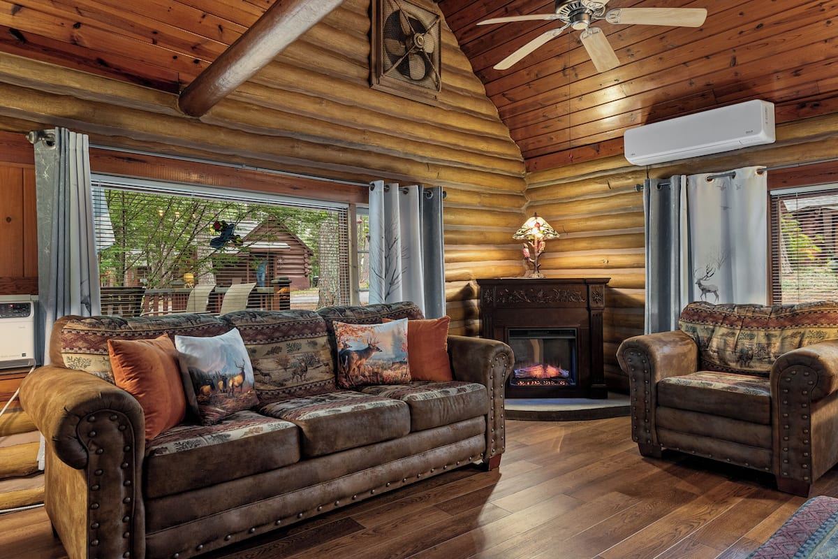 A log cabin interior with a leather sofa, fireplace, and large windows.