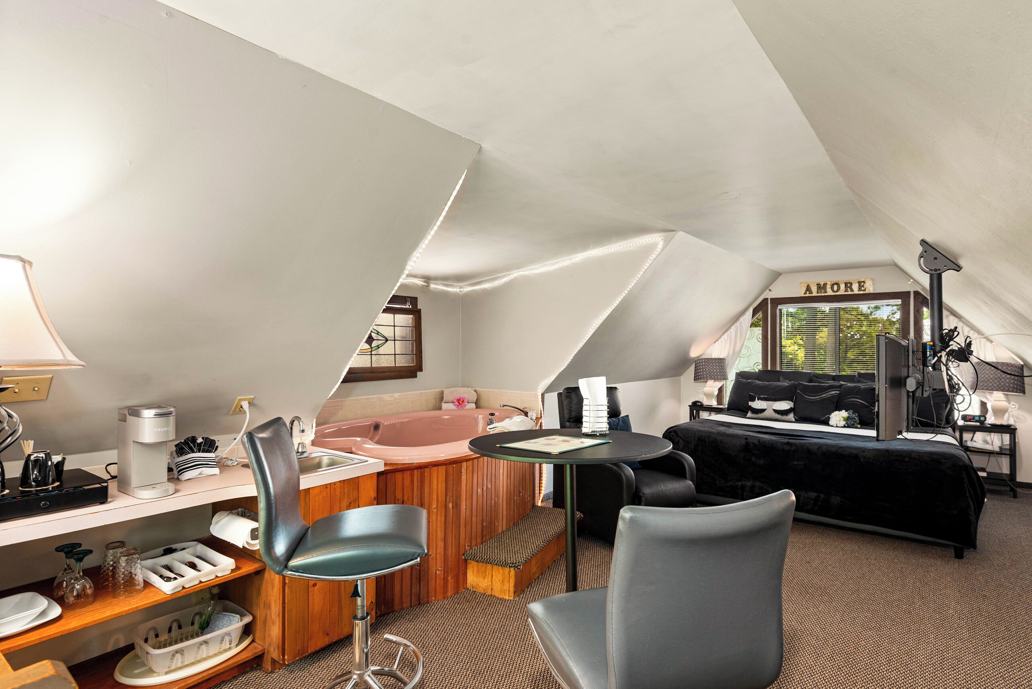 A cozy, well-lit room with a wooden desk, a comfortable chair, a small table, a sofa, and a bathtub.