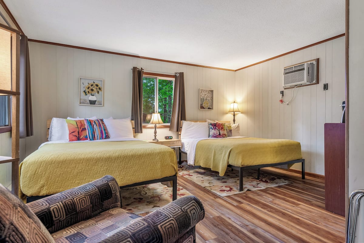 A room with two beds, a sofa, a window with curtains, and a wall-mounted air conditioner.