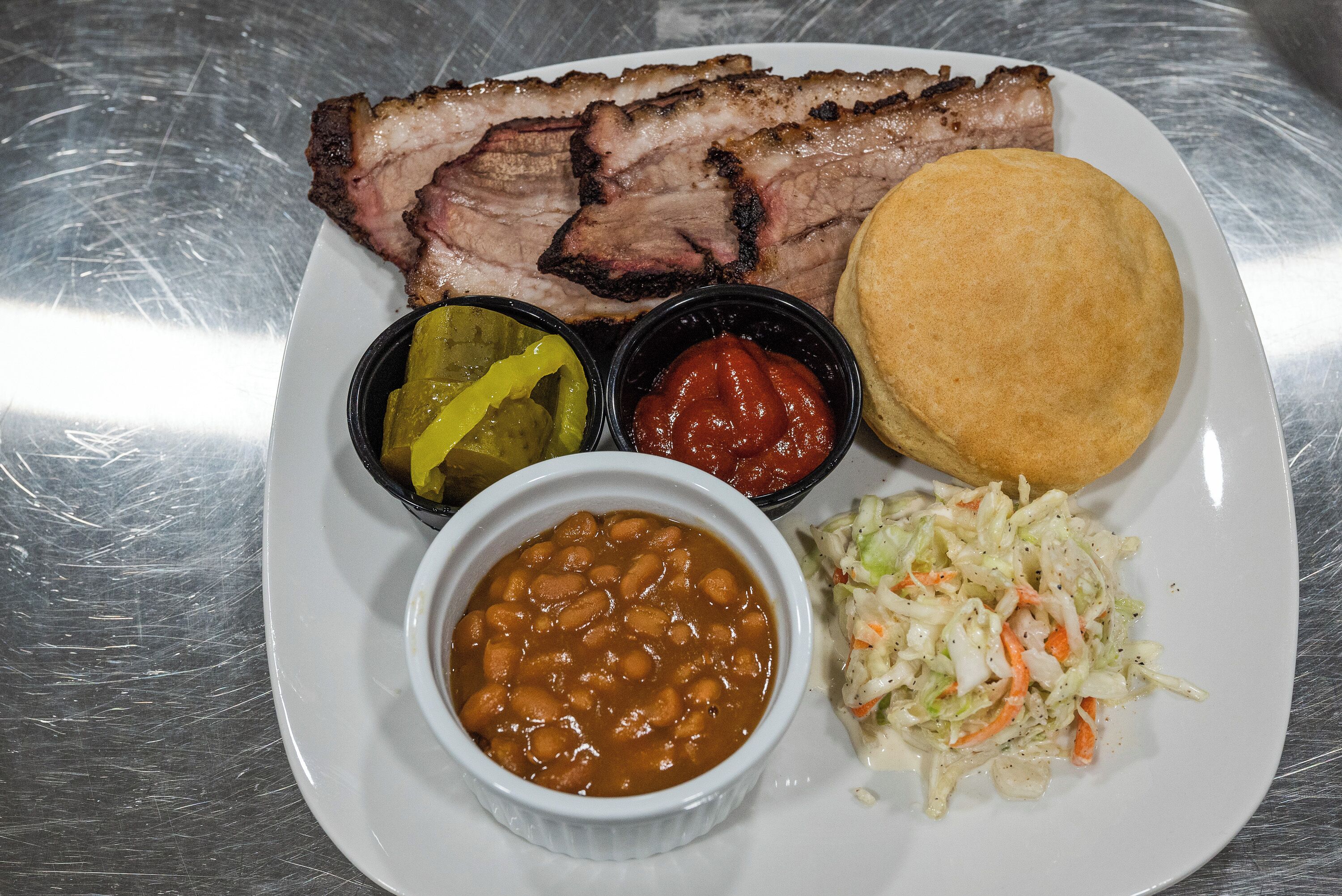 Un plato con carne a la parrilla, frijoles, ensalada de repollo, pepinillos y salsas.