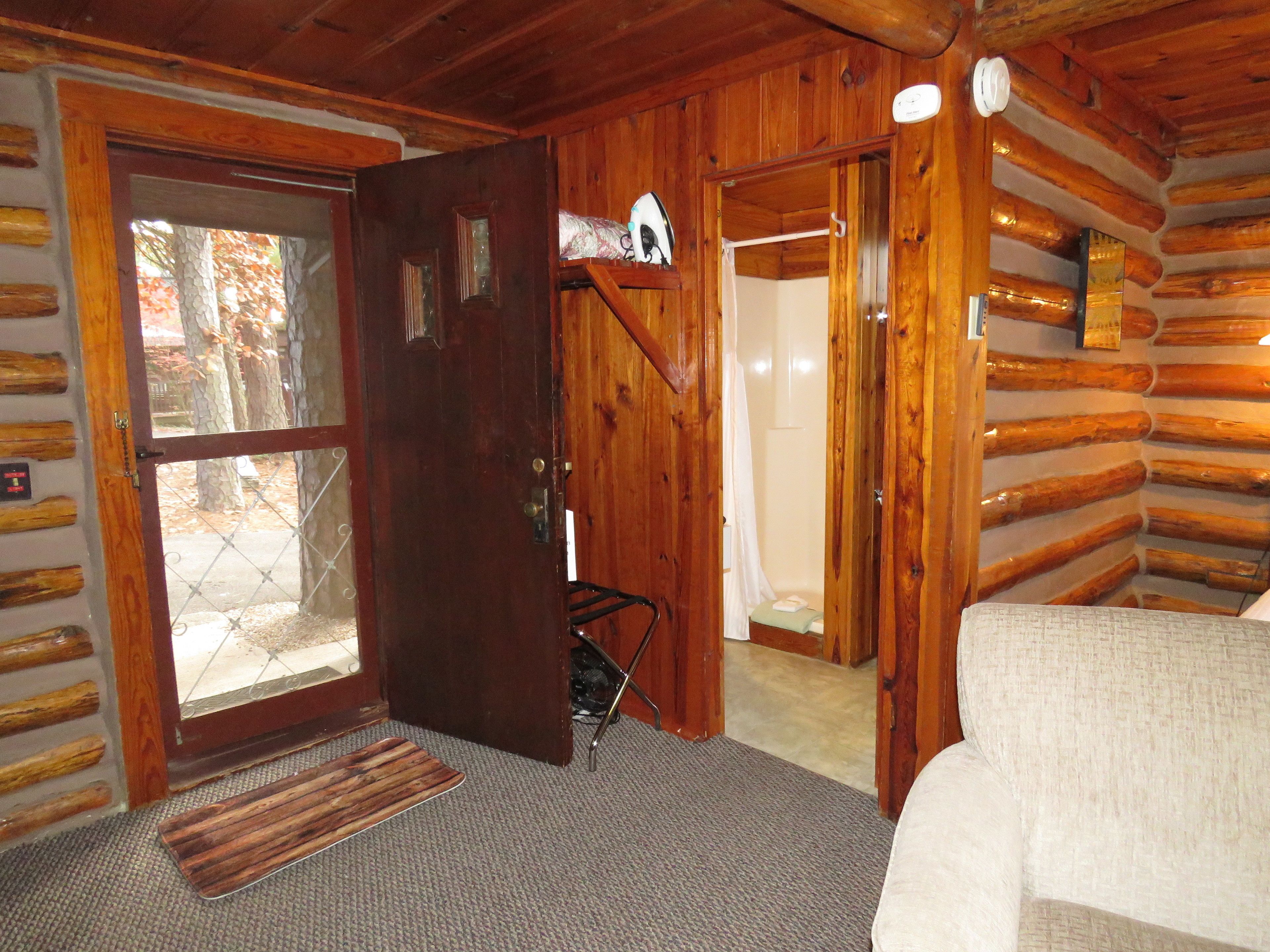 L'intérieur d'une cabane en rondins, avec une porte en bois, une petite marche menant à la salle de bain et un lit recouvert d'une couverture blanche.