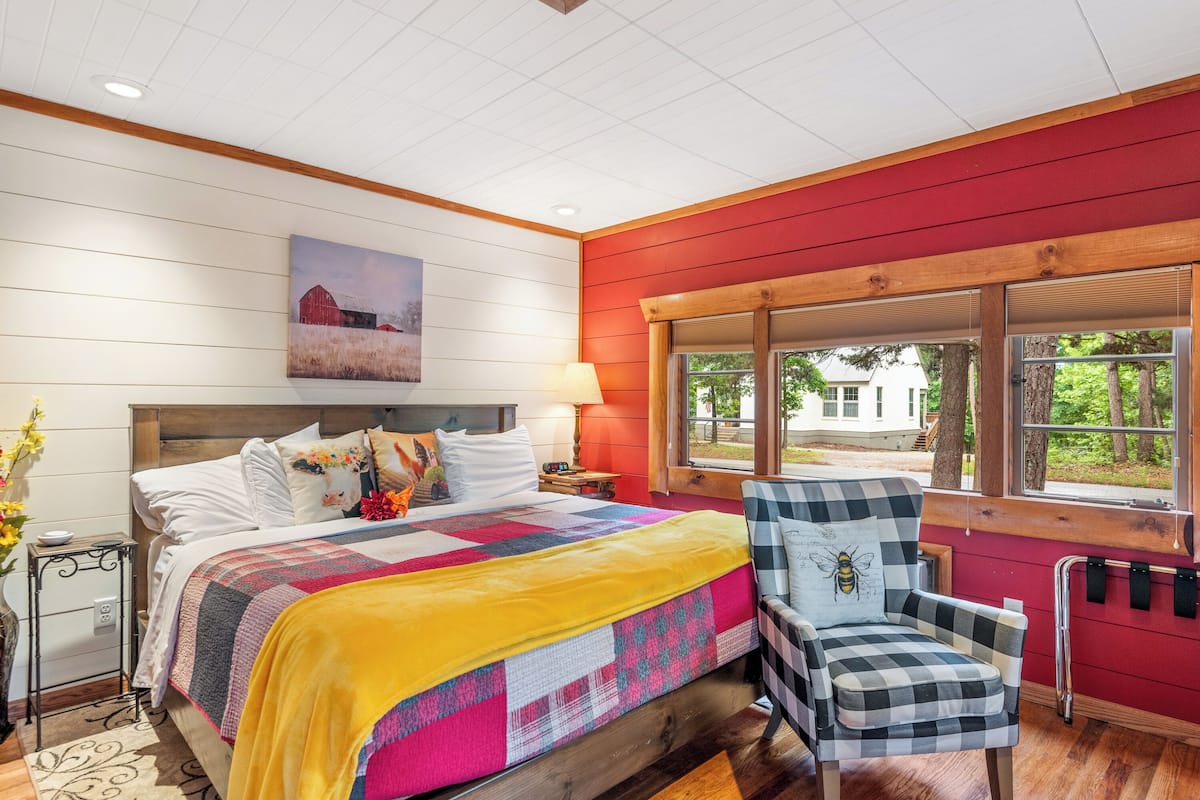 A bedroom with a large bed, a chair, a window, and a painting on the wall.
