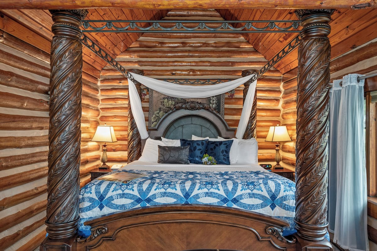 A log cabin-style bedroom with a four-poster bed, wooden beams, and a fireplace.