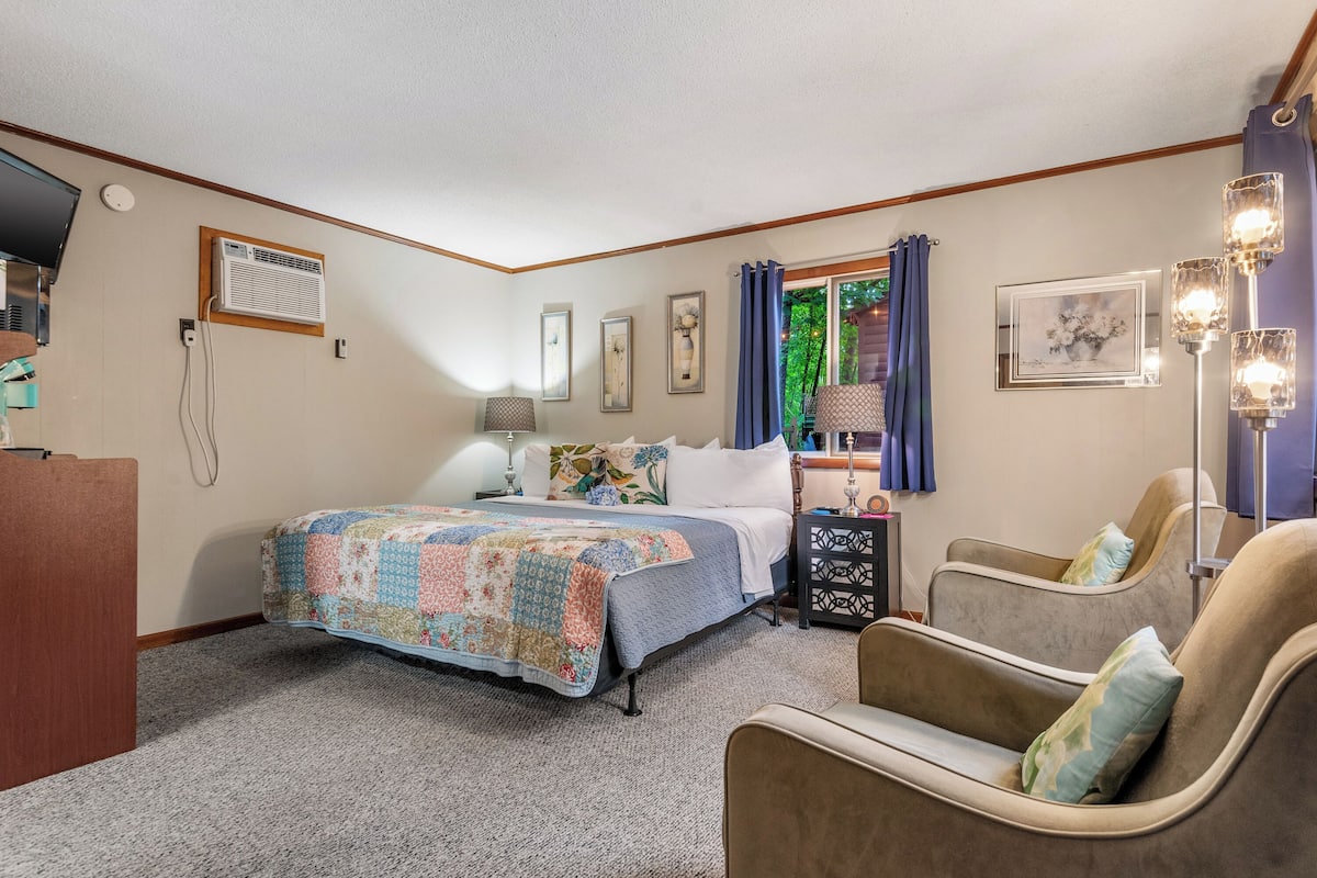 A bedroom with a bed, a desk, a chair, a lamp, and a window with curtains.
