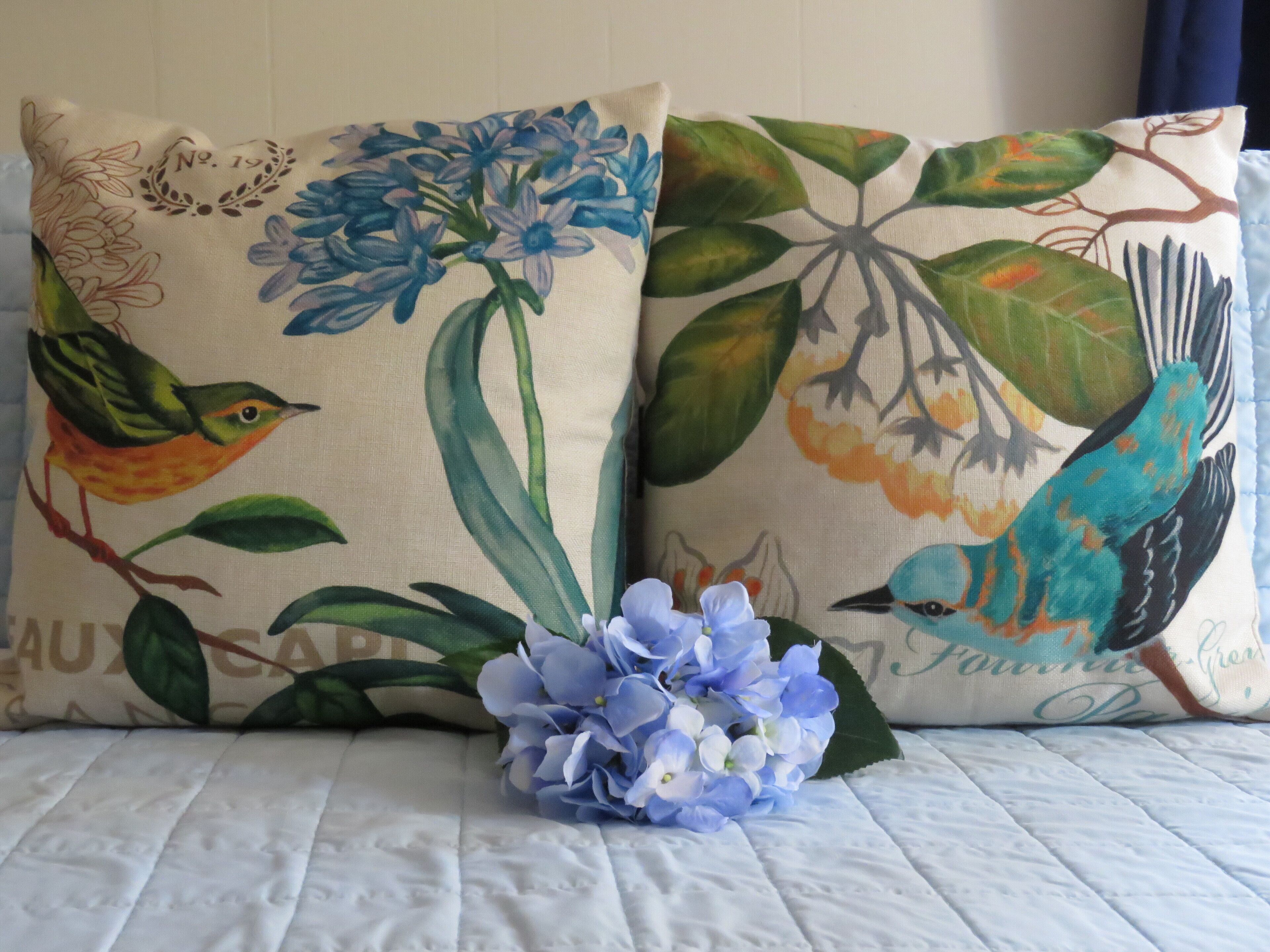 Deux oreillers ornés de motifs floraux et d’oiseaux, posés sur un lit.