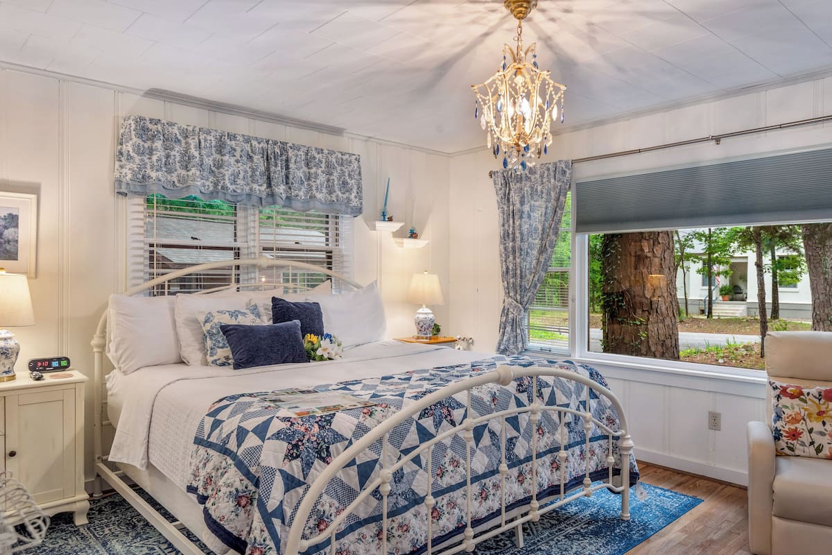 A bedroom with a bed, nightstand, lamp, and a view of the outdoors.