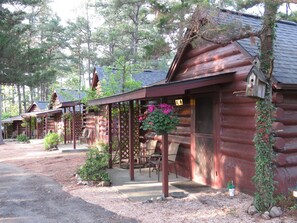 A row of log cabins with outdoor seating and hanging flower baskets. - Tall Pines Inn (Eureka Springs)