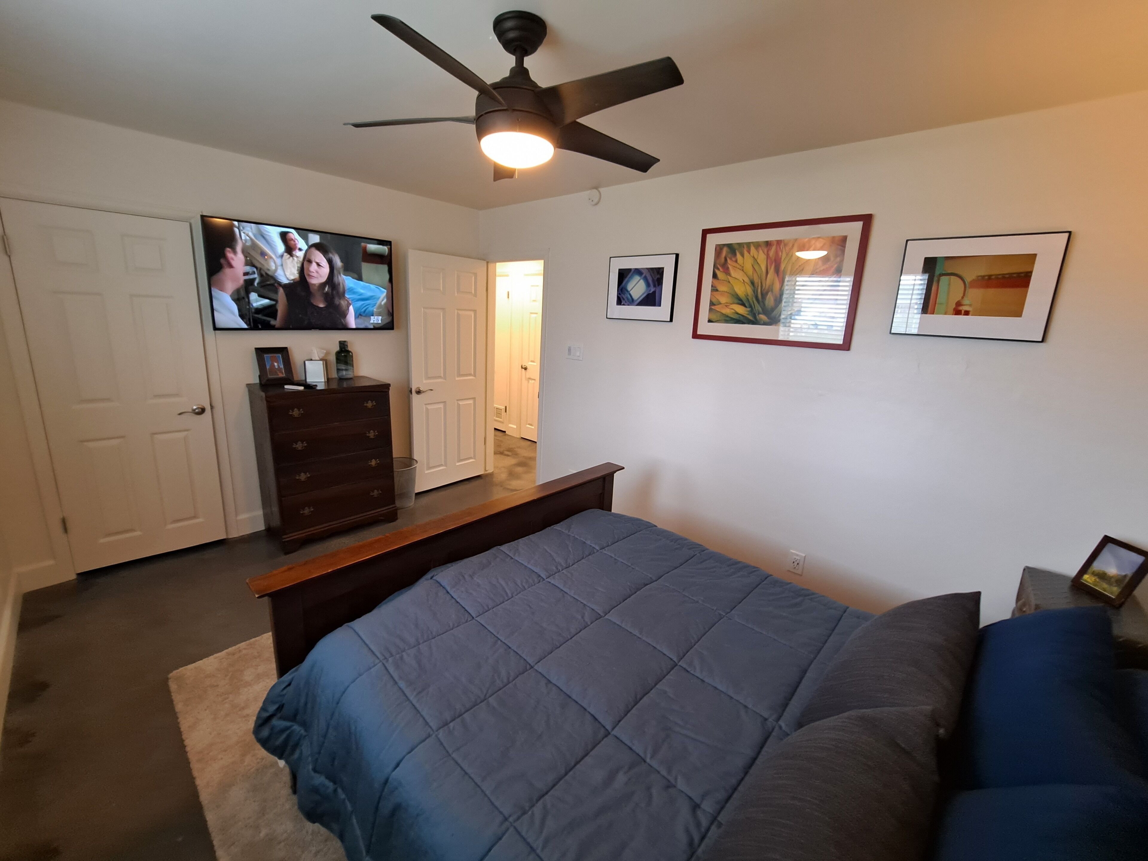 A bedroom with a bed, a dresser, a television, and framed pictures on the wall.