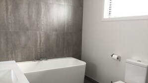 A bathroom with a bathtub, toilet, and a window with blinds. - Northlake Wanaka New Zealand. House to let in Ski Season. (Wanaka)