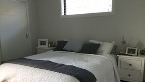 A bedroom with a bed, bedside tables, a nightstand, a window, and a wooden bench. - Northlake Wanaka New Zealand. House to let in Ski Season. (Wanaka)