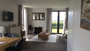 A modern living room with a fireplace, a television, and a large window offering a view of the outdoors. - Northlake Wanaka New Zealand. House to let in Ski Season. (Wanaka)