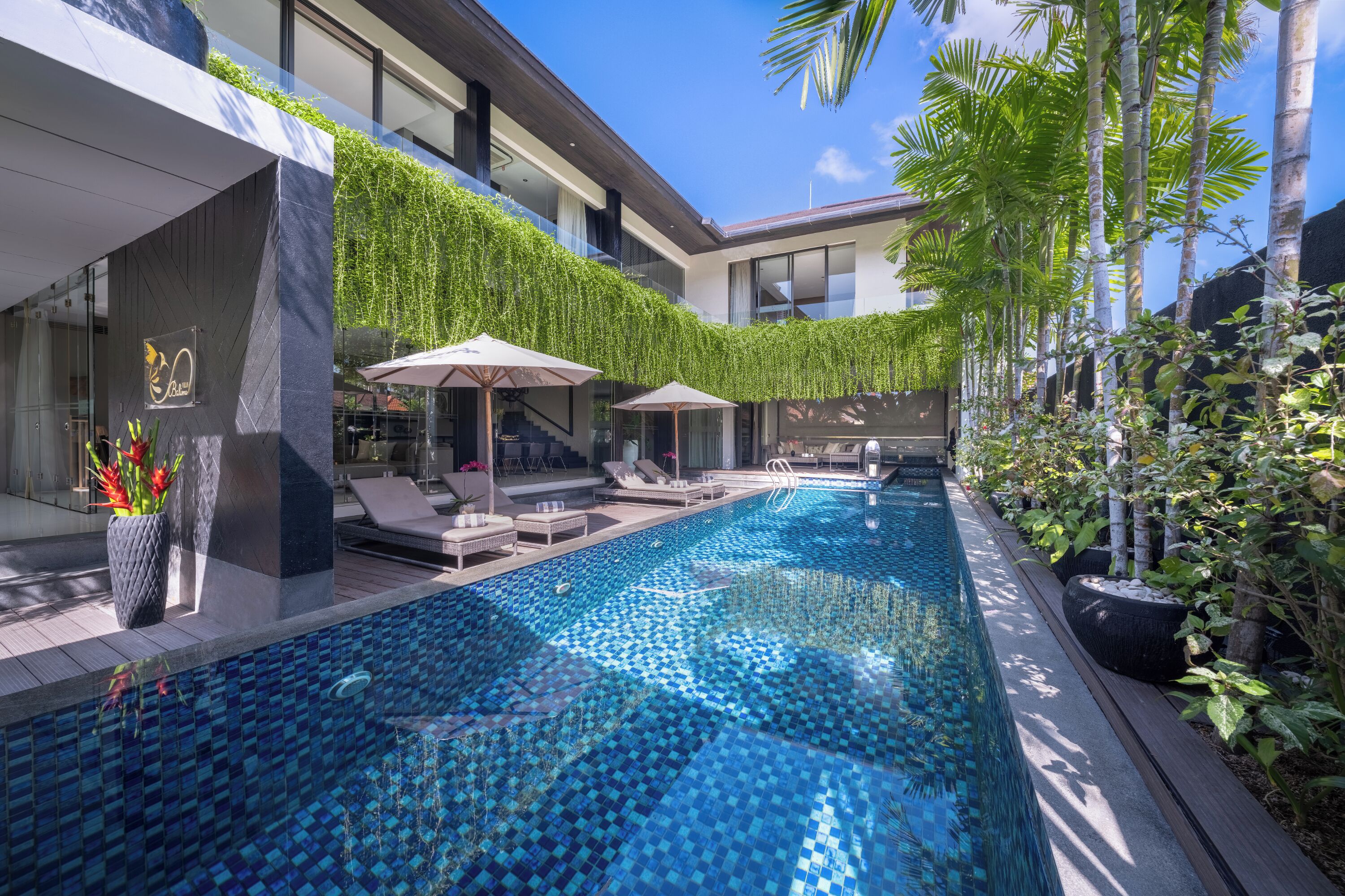 Un hotel moderno con piscina infinita en la azotea, sillones de descanso y un exuberante jardín verde.