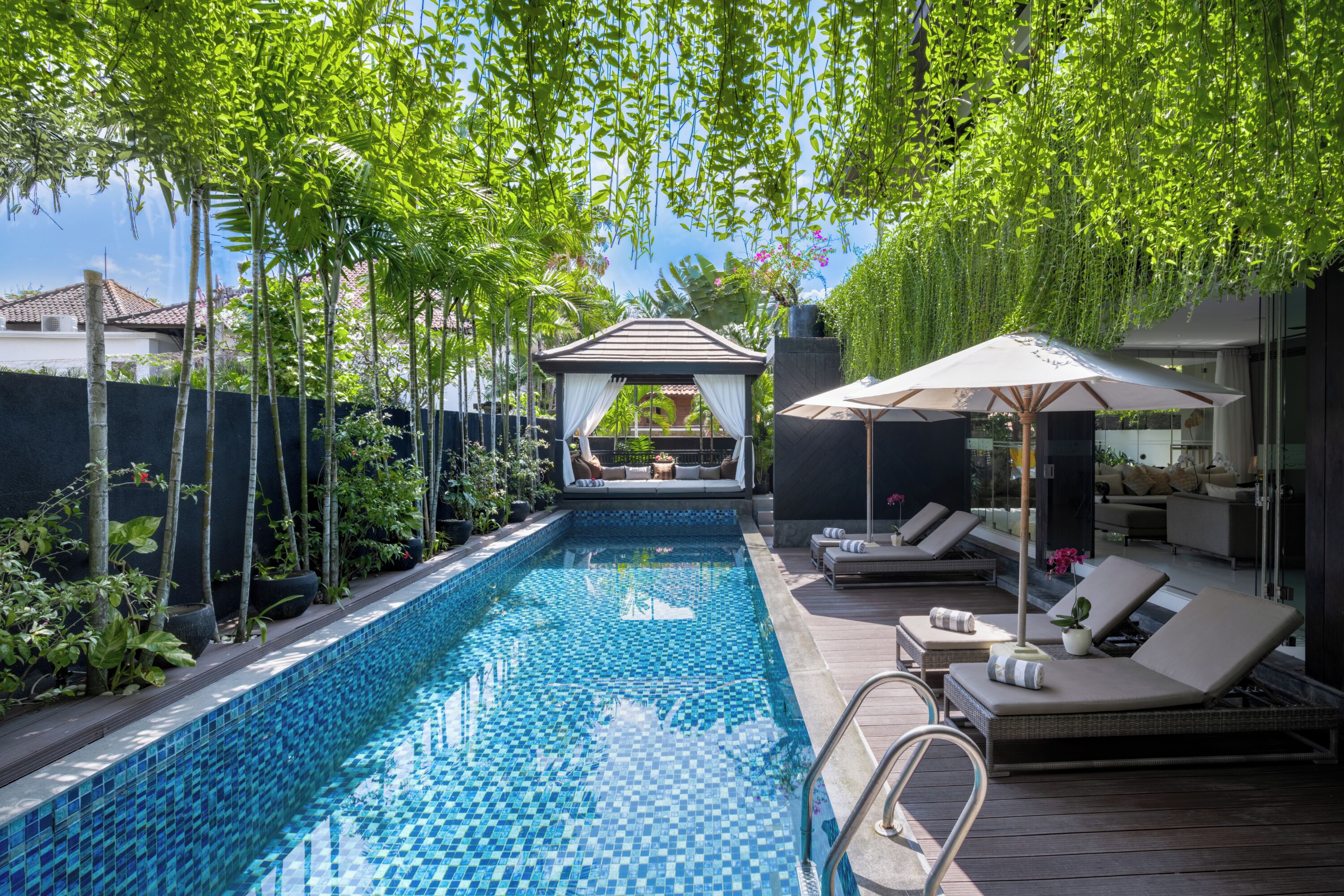 A swimming pool with a tiled edge, surrounded by lounge chairs and a covered seating area.
