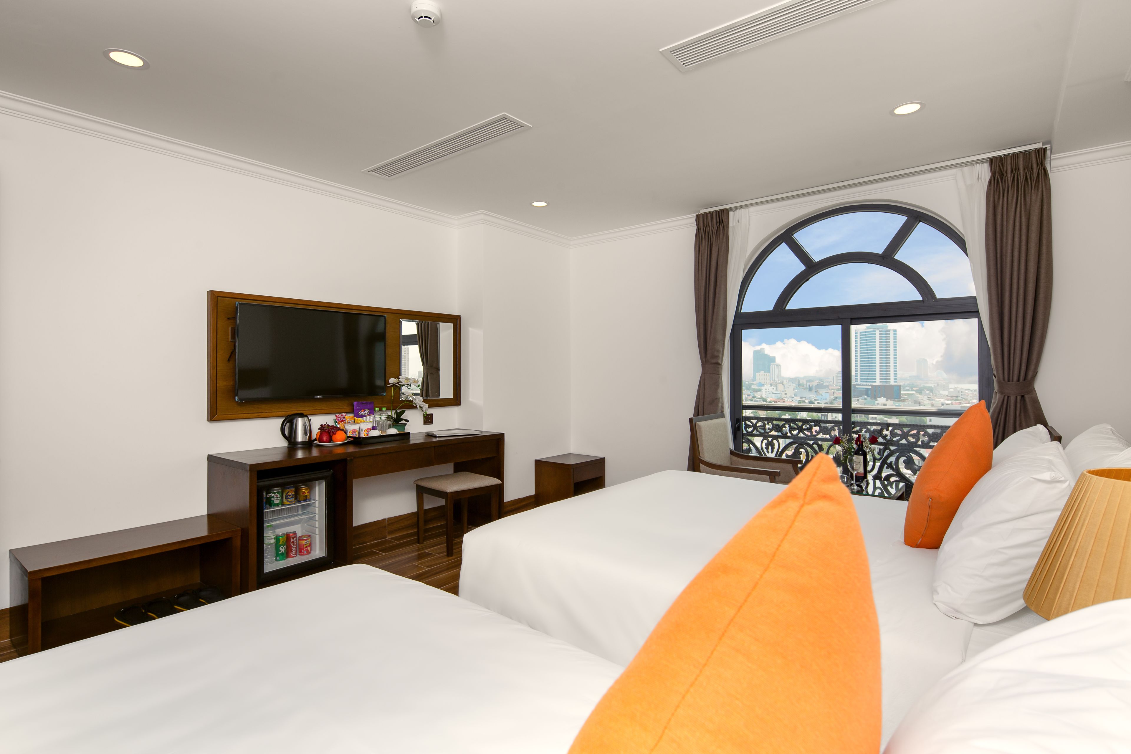 A hotel room with two beds, a TV, a minibar, and a window with a city view.