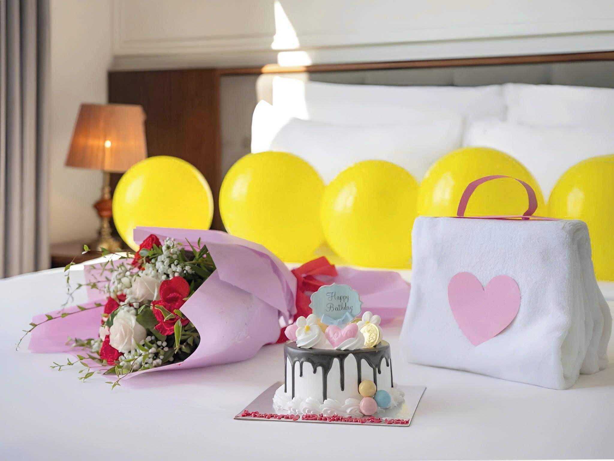A bed with a bouquet of flowers, a cake, and a gift bag.
