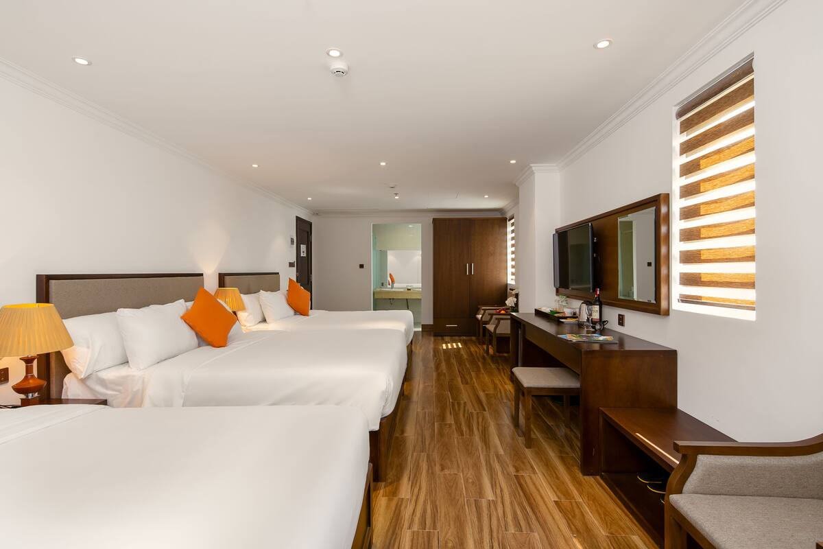 A hotel room with three beds, a desk, a chair, a TV, and a mirror.