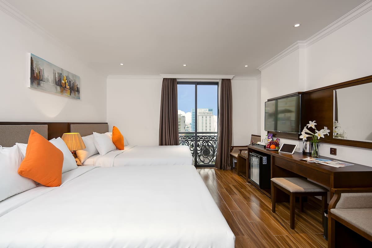 A hotel room with two beds, a desk, a TV, and a balcony with a city view.