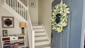 A staircase leading to a second floor, a console table with books and decorative items, and a door with a wreath.