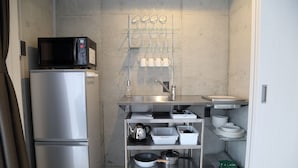 Una kitchenette compacta con refrigerador de acero inoxidable, microondas y un lavamanos pequeño.