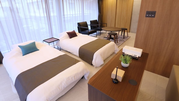 Habitación de hotel con dos camas, un escritorio, una silla y una mesita.