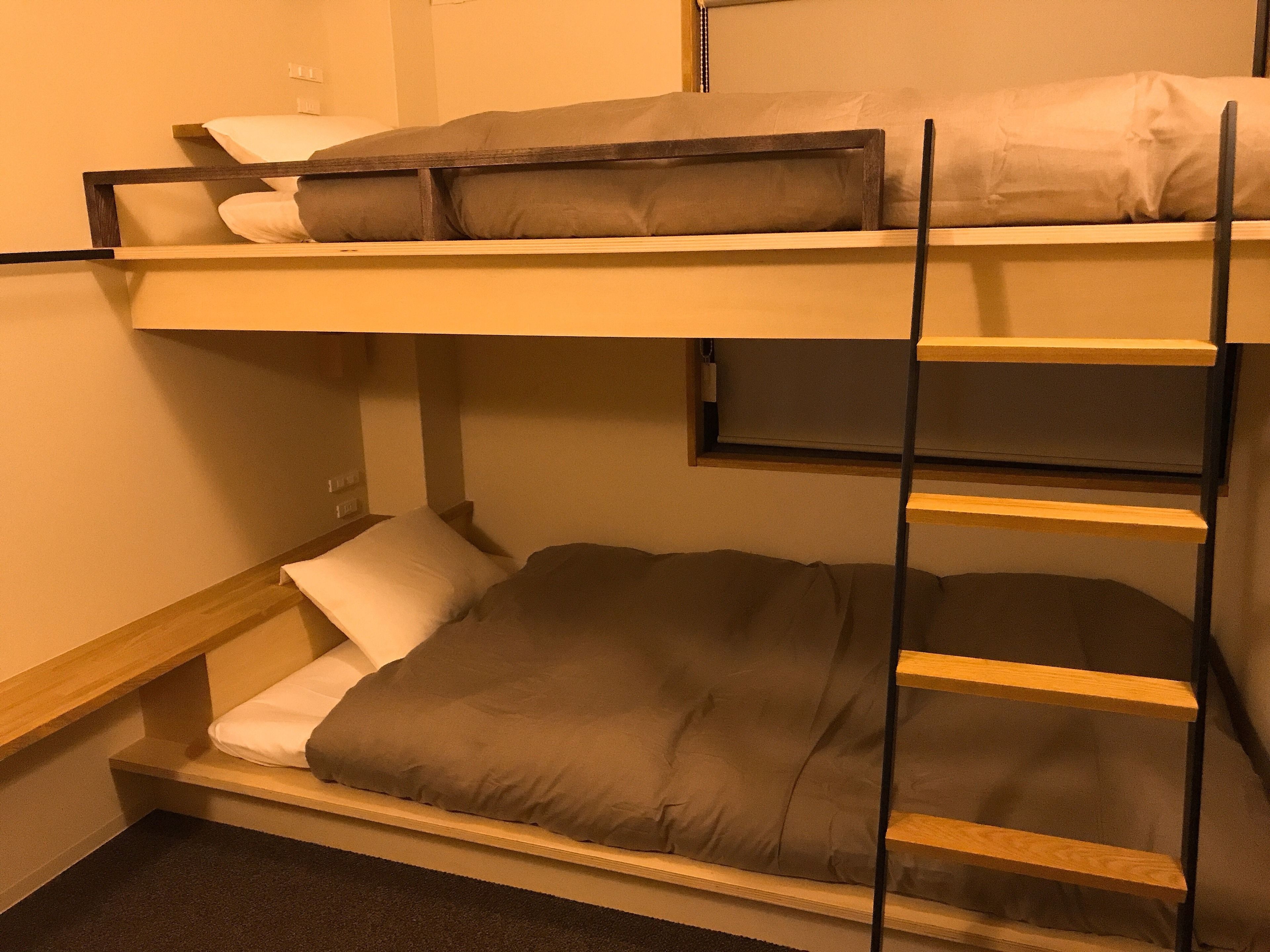 A bunk bed with a ladder, a small window, and a power outlet on the wall.