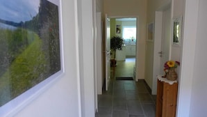 Un couloir doté d’un sol carrelé, un buffet en bois orné d’un vase de fleurs et une porte donnant sur une pièce avec une fenêtre.