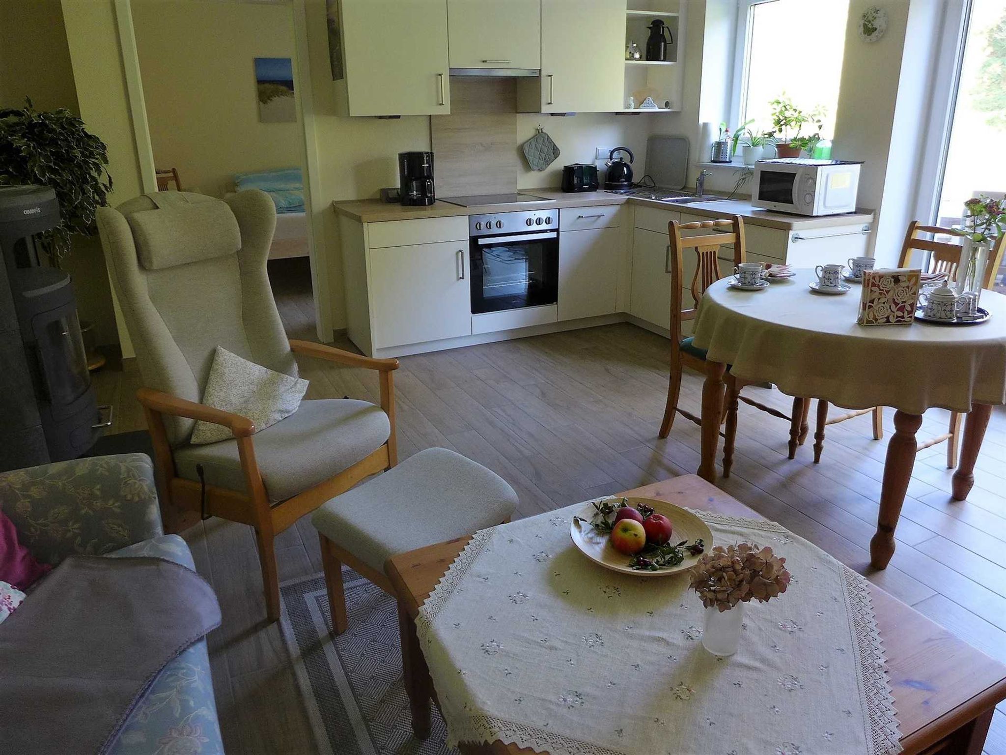 A cozy living room with a sofa, a dining table with a lace tablecloth, and a kitchen area with a stove and microwave.