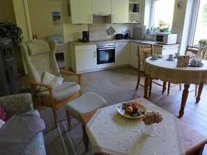 Una sala de estar acogedora con un sofá, una mesa de comedor con mantel de encaje y una zona de cocina con estufa y microondas.