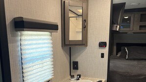Casa de banho compacta numa caravana, com lavatório, espelho e persianas.