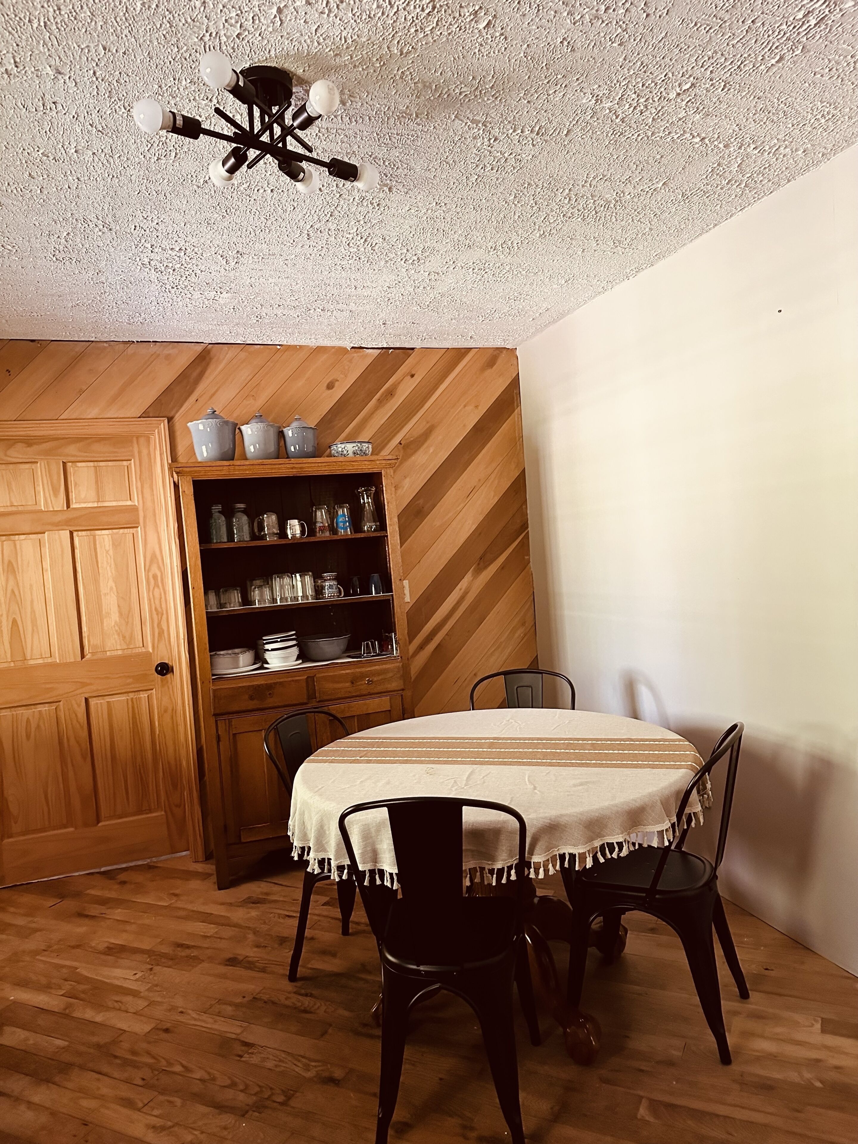 A dining area with a wooden table and chairs, a ceiling fan, and a wooden cabinet with kitchenware.