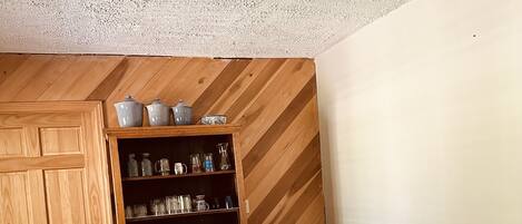 A dining area with a wooden table and chairs, a ceiling fan, and a wooden cabinet with kitchenware.