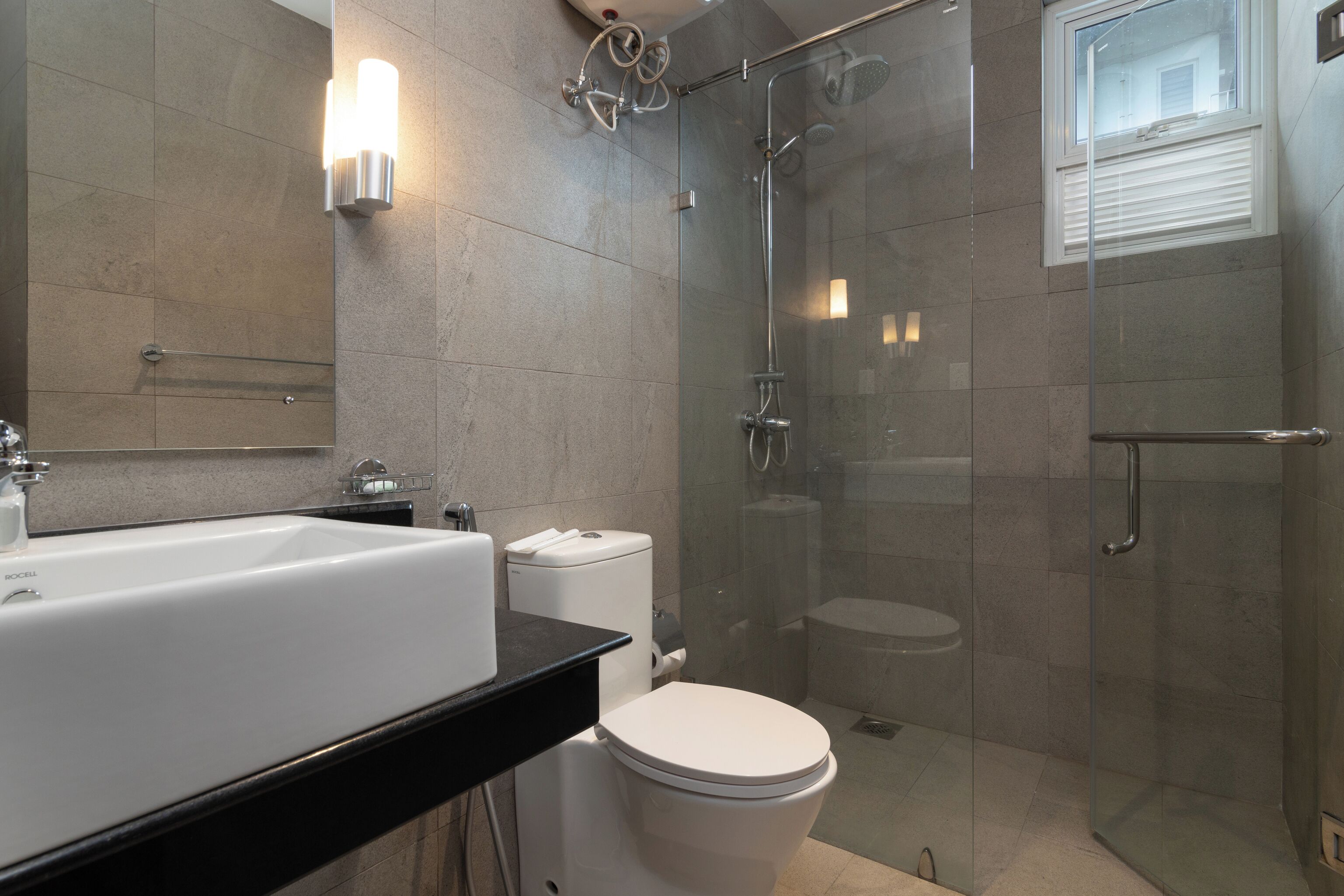 Un baño moderno con ducha de vidrio, inodoro blanco y lavamanos grande.
