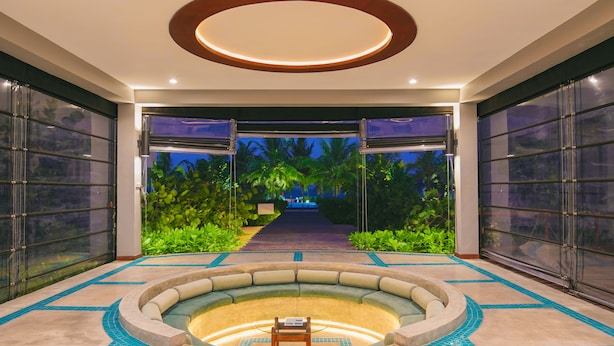 Un vestíbulo espacioso con una zona de estar circular, un acceso por puerta de vidrio y vistas a un jardín tropical por la noche.