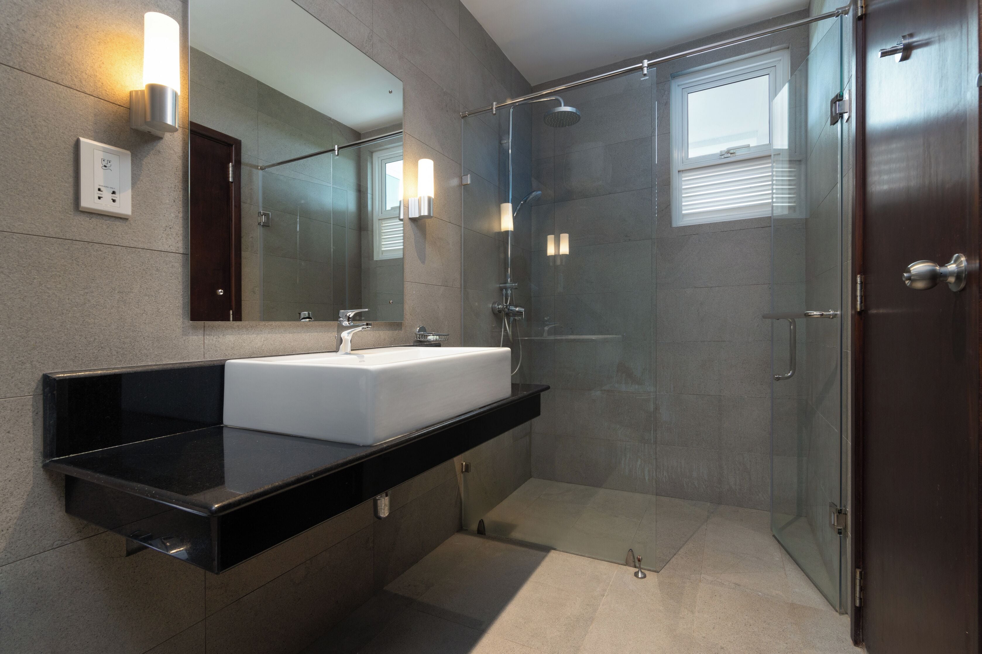 A modern bathroom with a glass shower enclosure, a white sink, and a dark countertop.