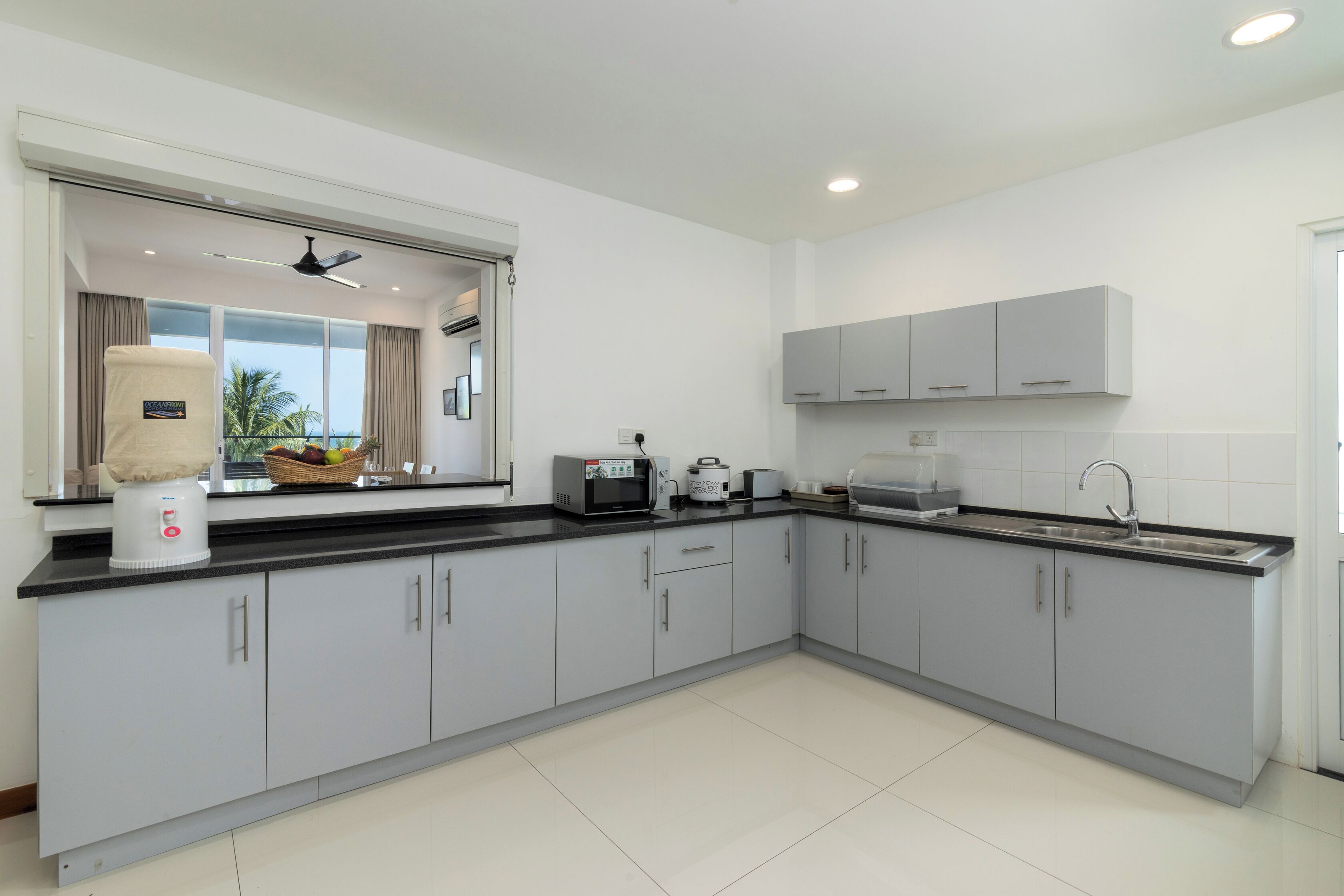 A modern kitchen with grey cabinets, a black countertop, and a window with curtains.