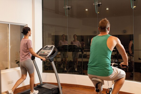 Un gimnasio con cintas de correr y bicicletas estáticas, amplias ventanas y un espejo que refleja el espacio.