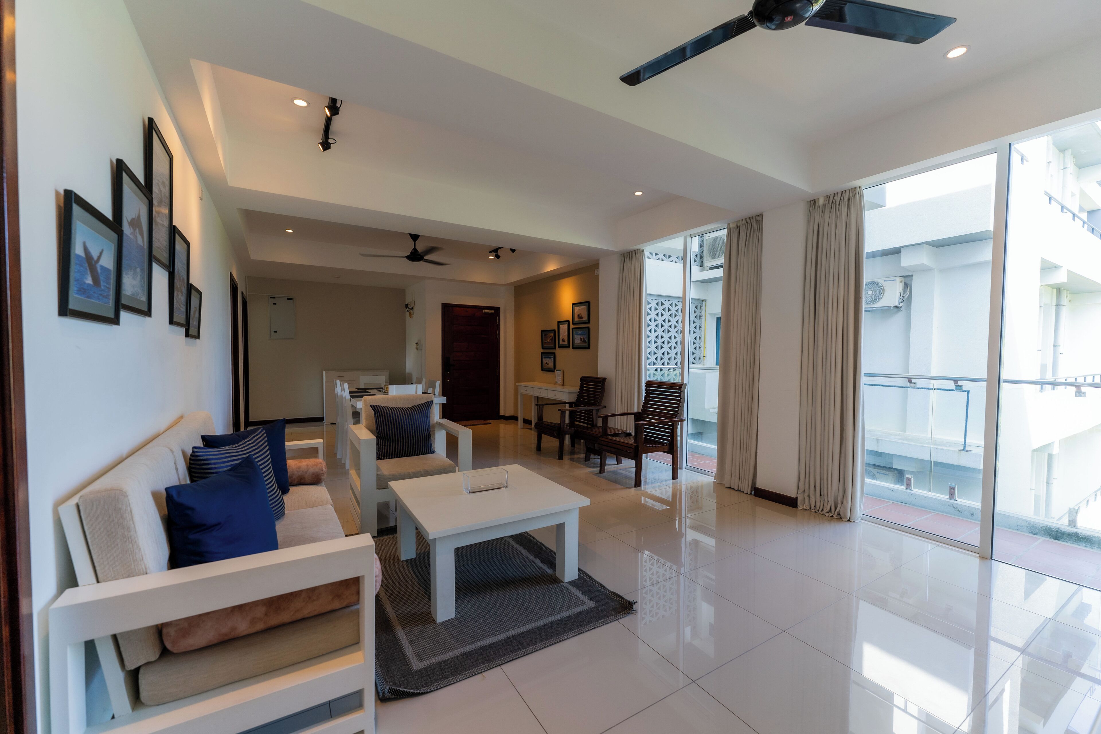 A spacious living area with a sofa, coffee table, and chairs. There is a balcony with a view of the outside.