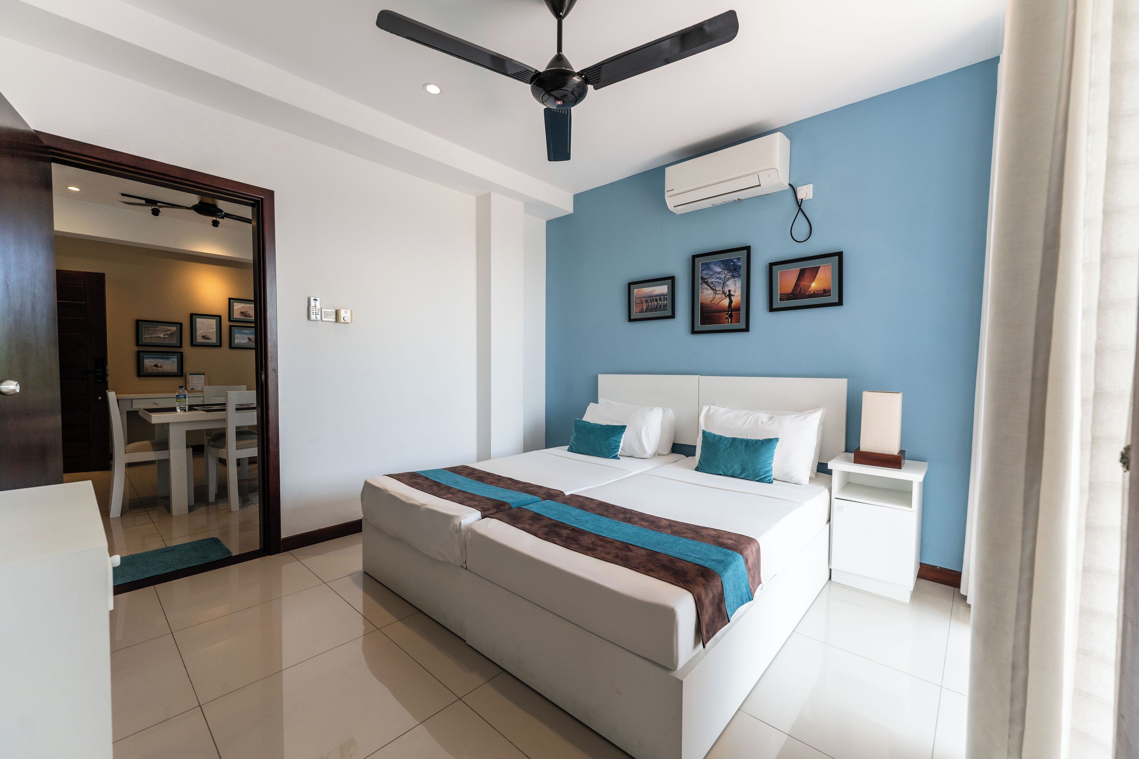 Una camera d'albergo con un letto grande, una ventola a soffitto, un condizionatore d'aria, un comodino e vista su una sala da pranzo.