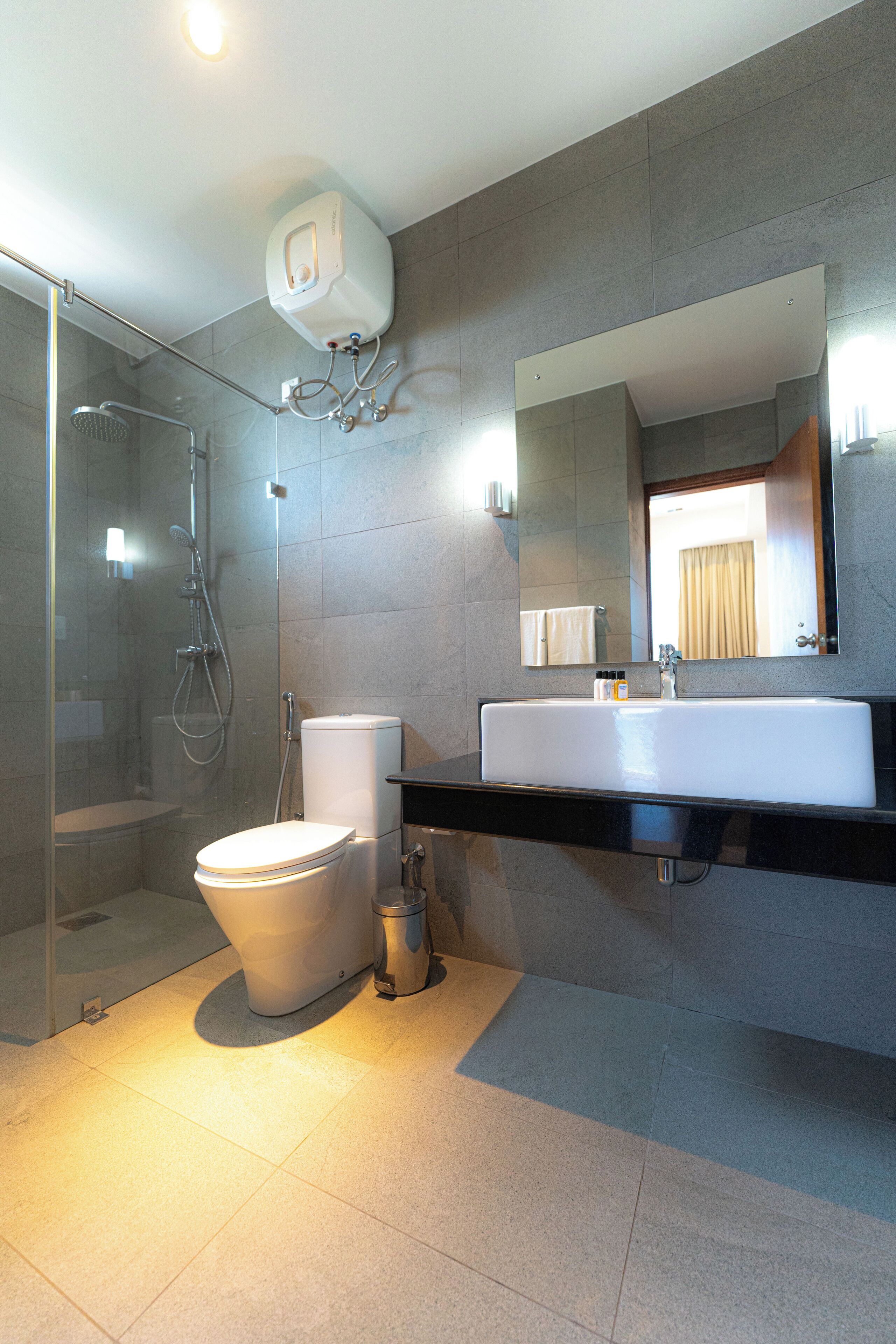 A modern bathroom with a glass-enclosed shower, a white toilet, and a large mirror above a black countertop.