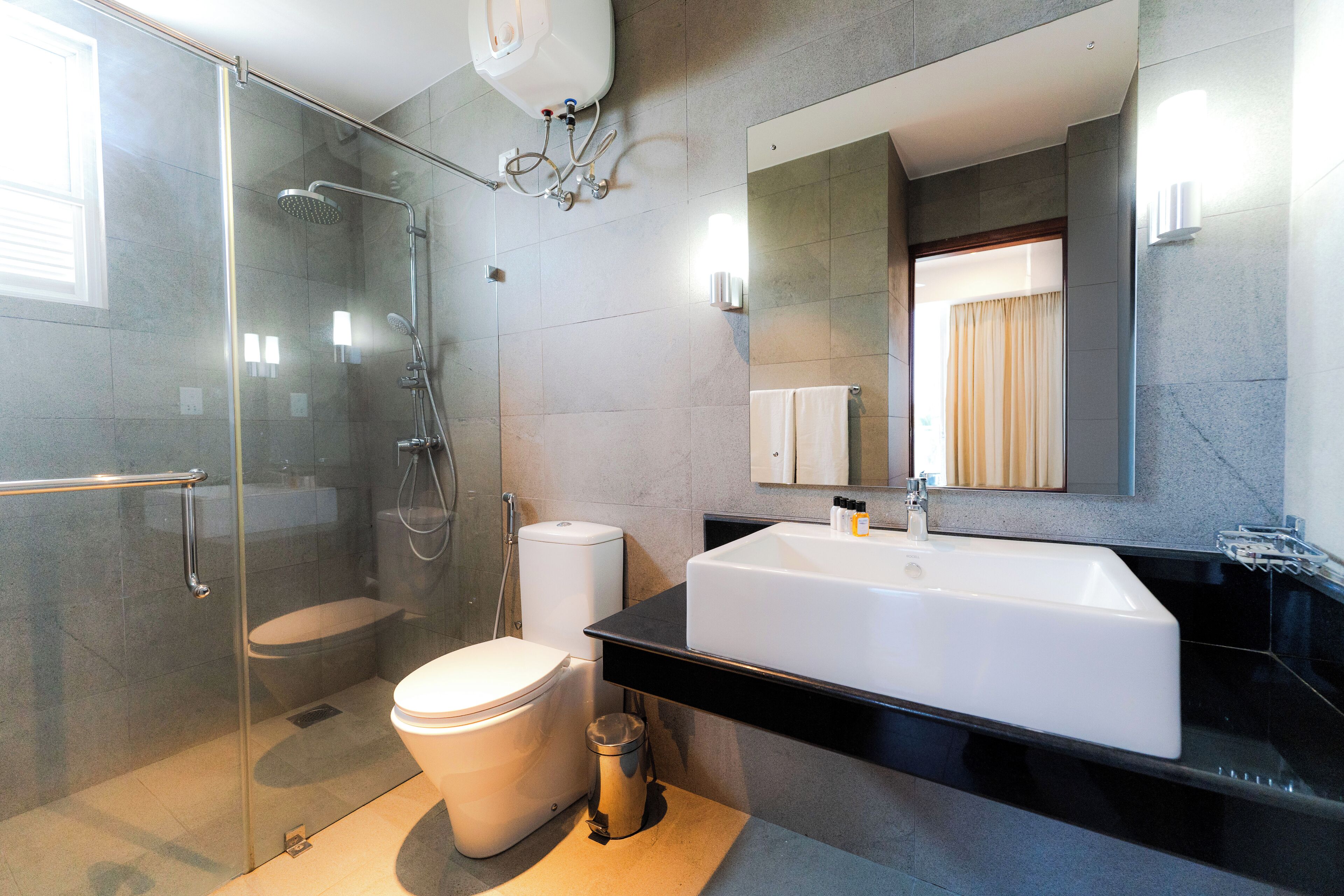 A modern bathroom with a glass-enclosed shower, a white toilet, a large white sink, and a mirror above the sink.