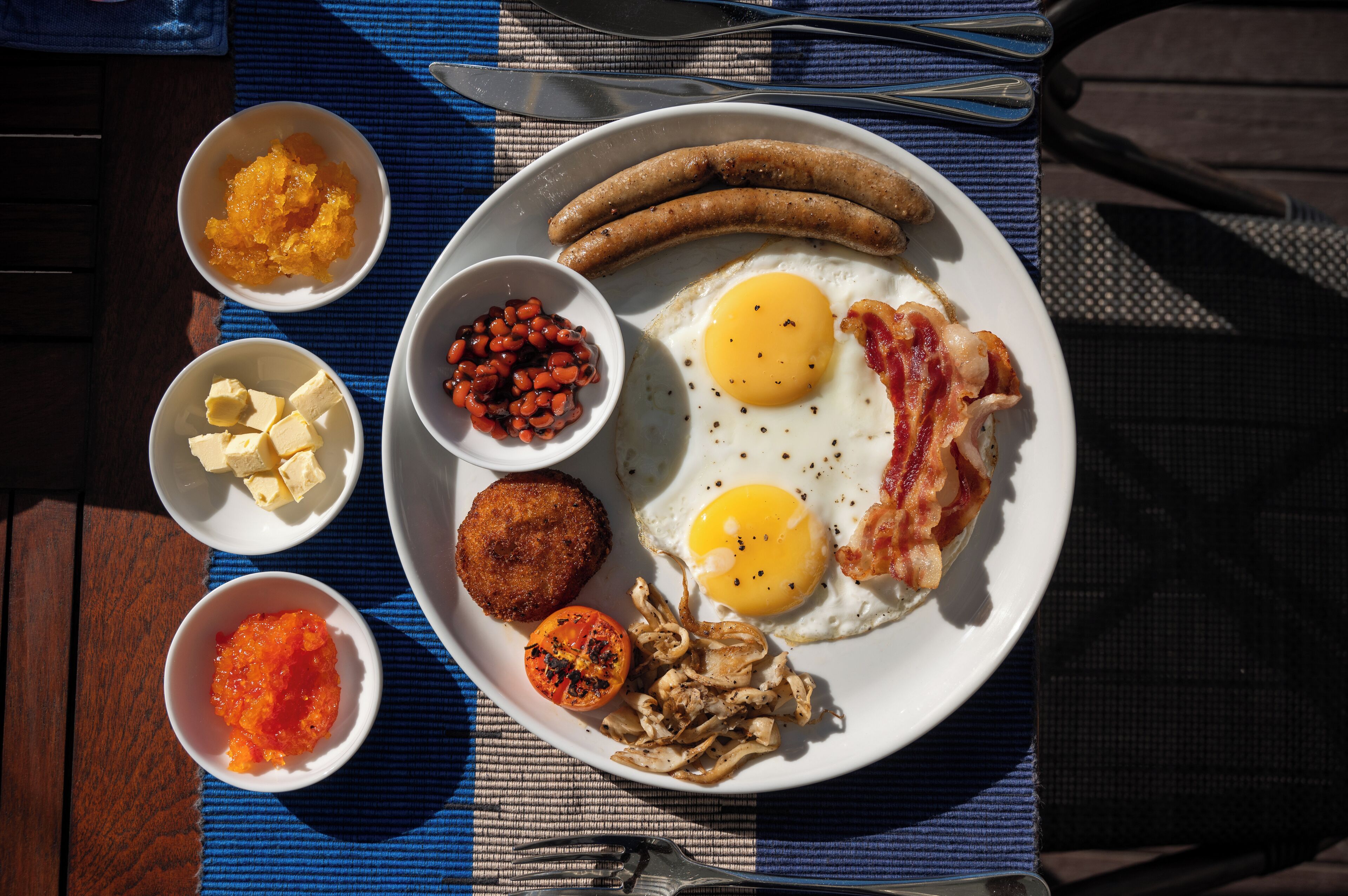 A breakfast plate with sausages, eggs, bacon, and various condiments.