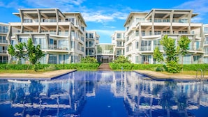 Un hotel moderno con piscina central, rodeado de exuberante vegetación y un cielo azul despejado.