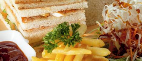 Un sándwich con lechuga y tomate sobre una tabla de madera, acompañado de papas fritas y una ensalada.