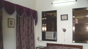 A bedroom with a bed, curtains, a wall-mounted air conditioner, a bedside table, and a mirror. - Blue Chip Guest House Kolkata (Kolkata)