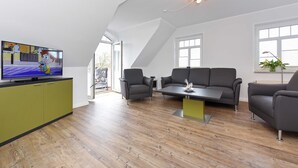 Una sala de estar moderna con televisor, sofás grises, una mesa de centro y un mueble verde.