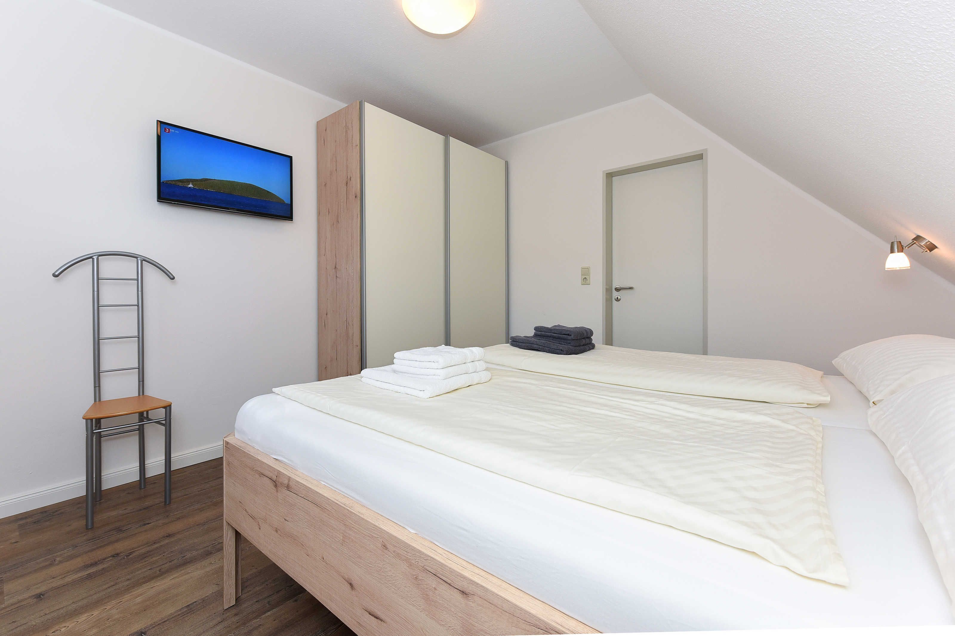 Ein Schlafzimmer mit einem Bett, einer Holzleiter, einem an der Wand montierten Fernseher und einer Tür.