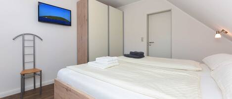 Ein Schlafzimmer mit einem Bett, einer Holzleiter, einem an der Wand montierten Fernseher und einer Tür.