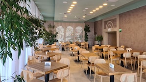 Un restaurant spacieux avec des tables et des chaises en bois, des luminaires au plafond et des panneaux décoratifs sur les murs.