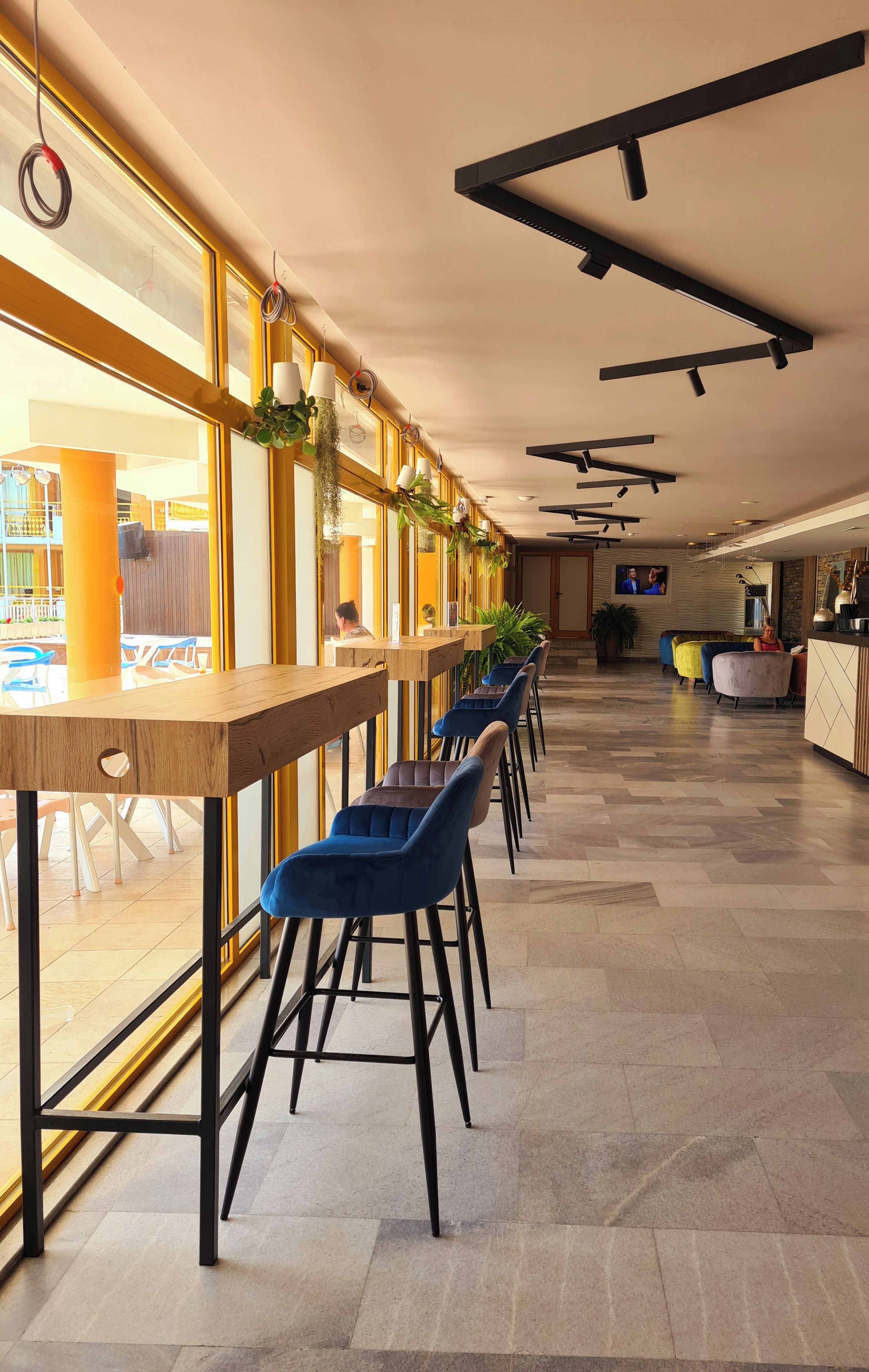 A modern interior with long tables and blue chairs, large windows, and a reception area.